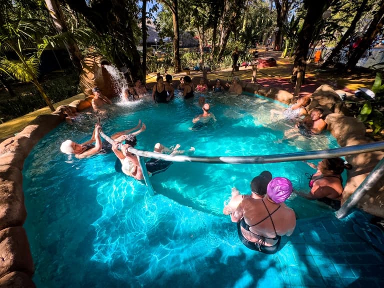 Piscina termal com temperatura mais elevada, vapor saindo da água e pessoas relaxando nas bordas.